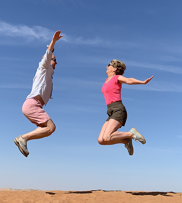 woman-man-jumping-desert-sand-blue-sky