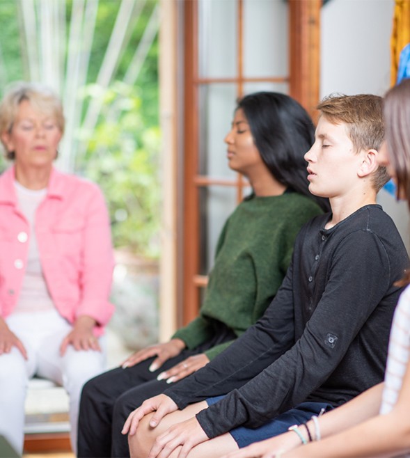 adolescents-sitting-on-a-chair-with-eyes-closed-meditating-with-teacher